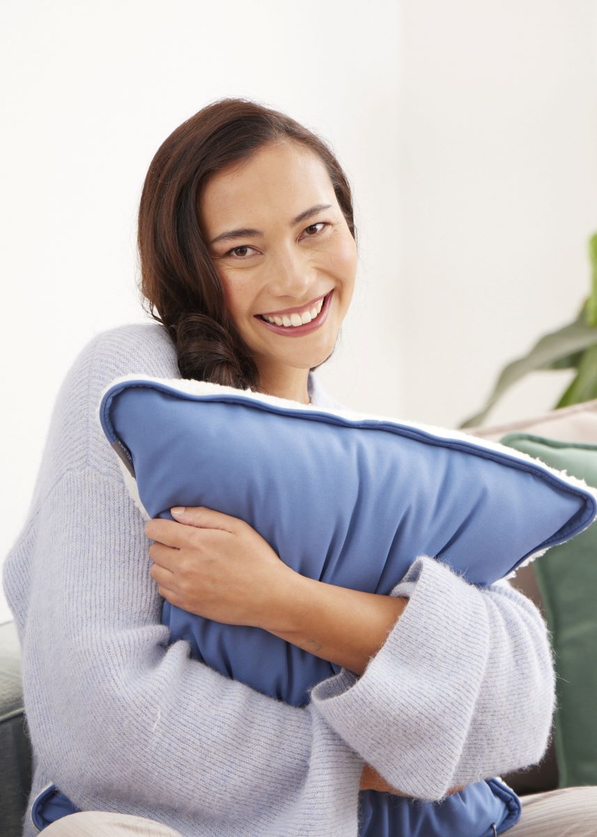 Woman hugging a blue medisana heated pad and enjoying soothing warmth.